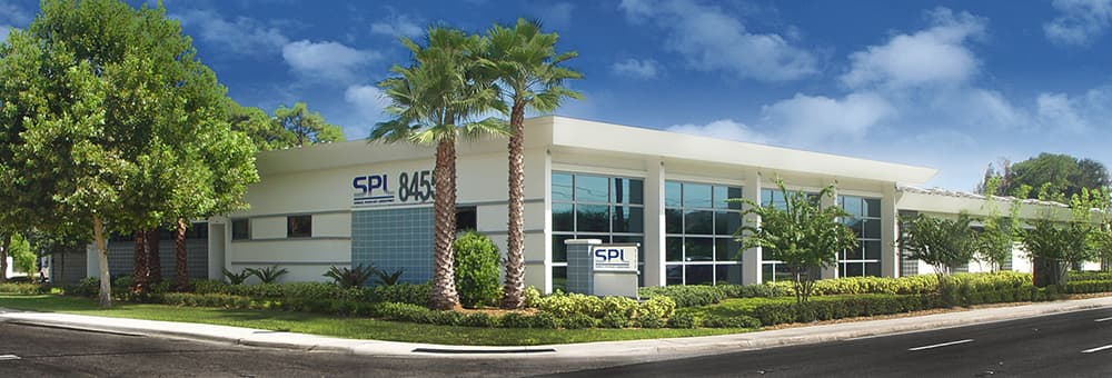 White building with glass on one site, palm trees out front, and SPL written on the site.