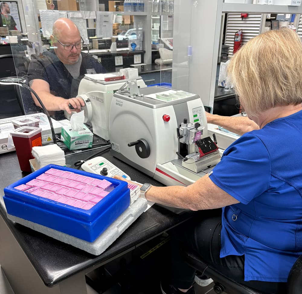 A table in the lab with two employees on either side working with desk size medical equipment.
